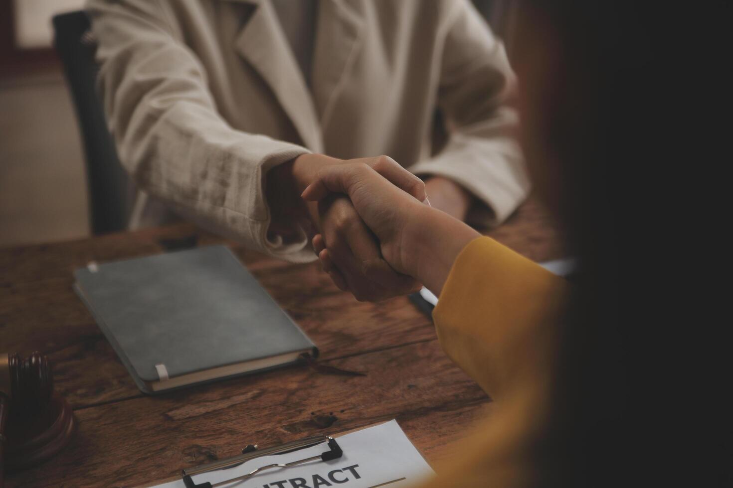 Lawyer shaking hands with a client making about documents, contracts, agreements, cooperation agreements with a female client at the lawyer's desk and a hammer at the table. photo