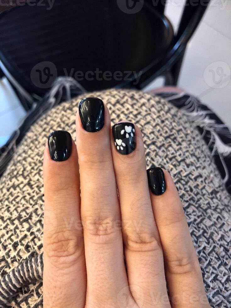 Close-up of a hand with black nail polish and white paw print nail art. photo