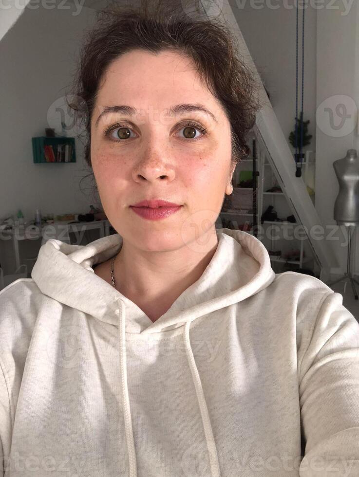 Selfie portrait of woman in cozy hoodie relaxing at home. Natural portrait in a modern domestic setting. Comfort in simplicity, everyday authenticity and serene domestic life concept photo
