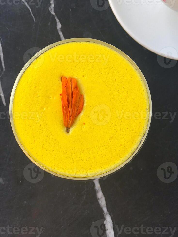Bright yellow vegan smoothie with alternative plant milk with delicate floral accent on marble table. Vibrant drink with rich color and elegant presentation. Coffee Shop photo