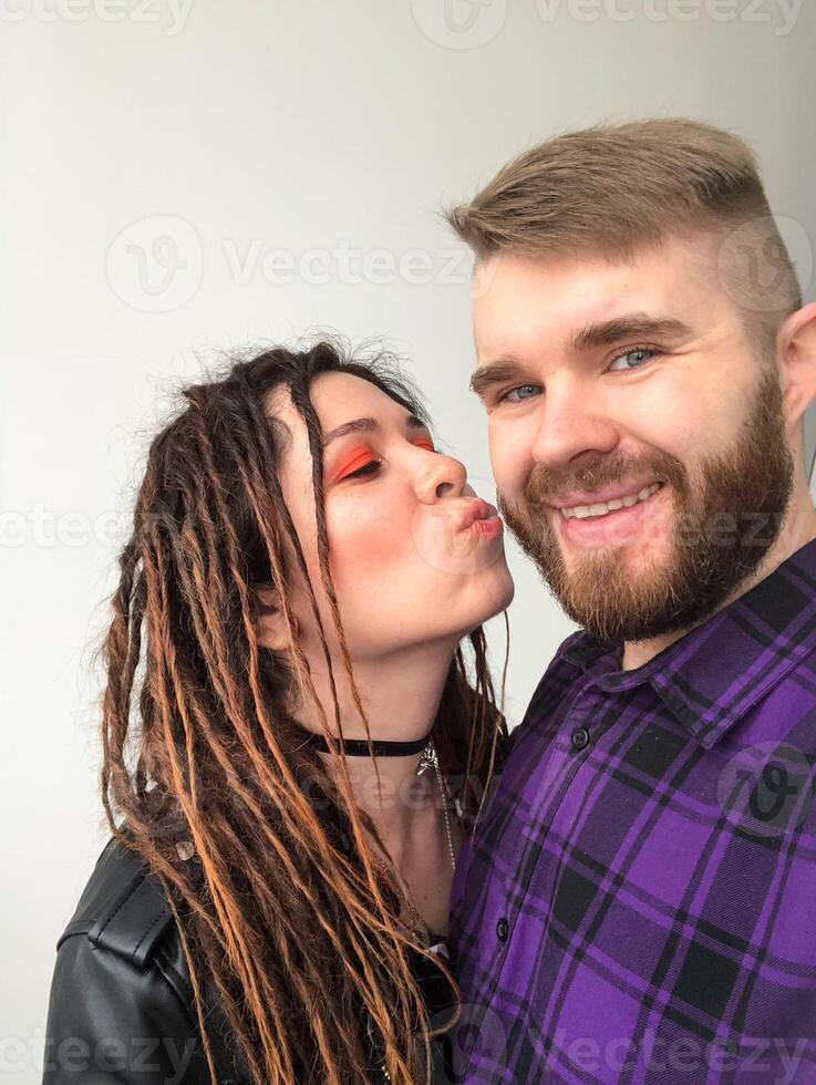 Cheerful Couple Sharing a Playful Moment. Joyful modern rock style female portrait. Woman with dreadlocks and grunge style clothing and make up kissing her boyfriend. photo