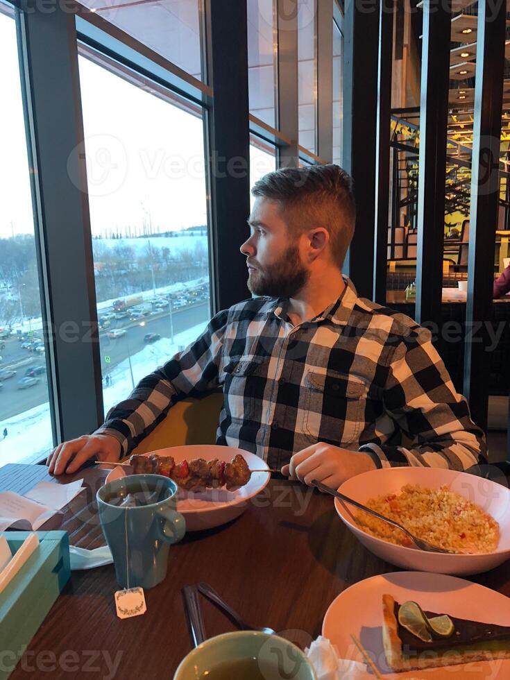 Man enjoying a cozy lunch in restaurant with a city view in winter season. Dining experience, cafe and winter comfort photo