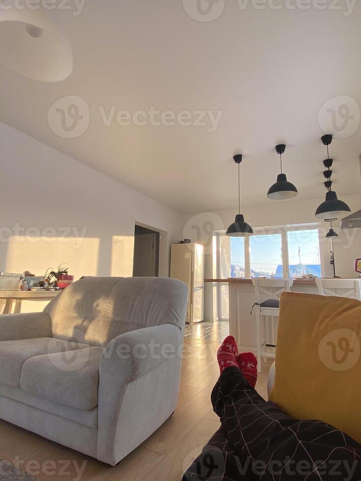 Female wears Christmas socks and relaxing on a cozy couch in a bright, modern living room with warm sunlight streaming through the windows. Contemporary interior design simplicity and comfort. photo