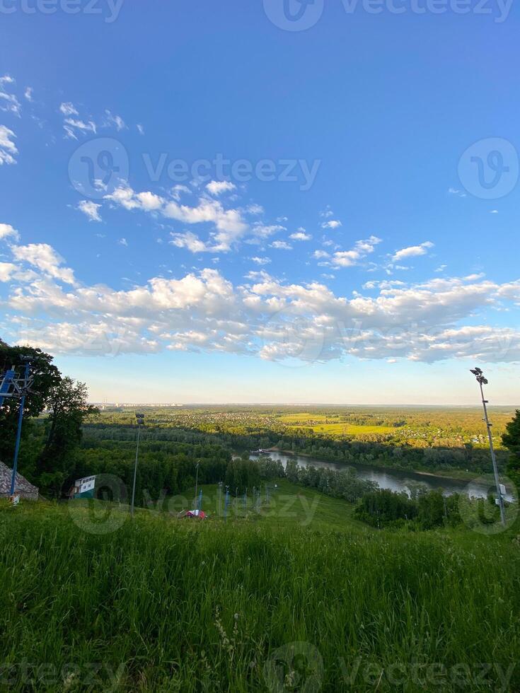 Scenic view of lush landscape with river and vast sky and the ski lift not work in summer. Panorama of nature captured from hilltop during serene summer day. photo