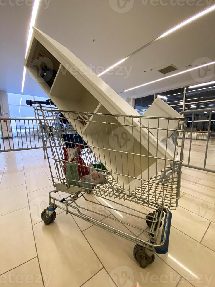 Large piece of furniture is precariously balanced in a shopping cart inside a spacious, modern mall. The unusual sight contrasts everyday shopping tasks with unexpected logistical challenges photo