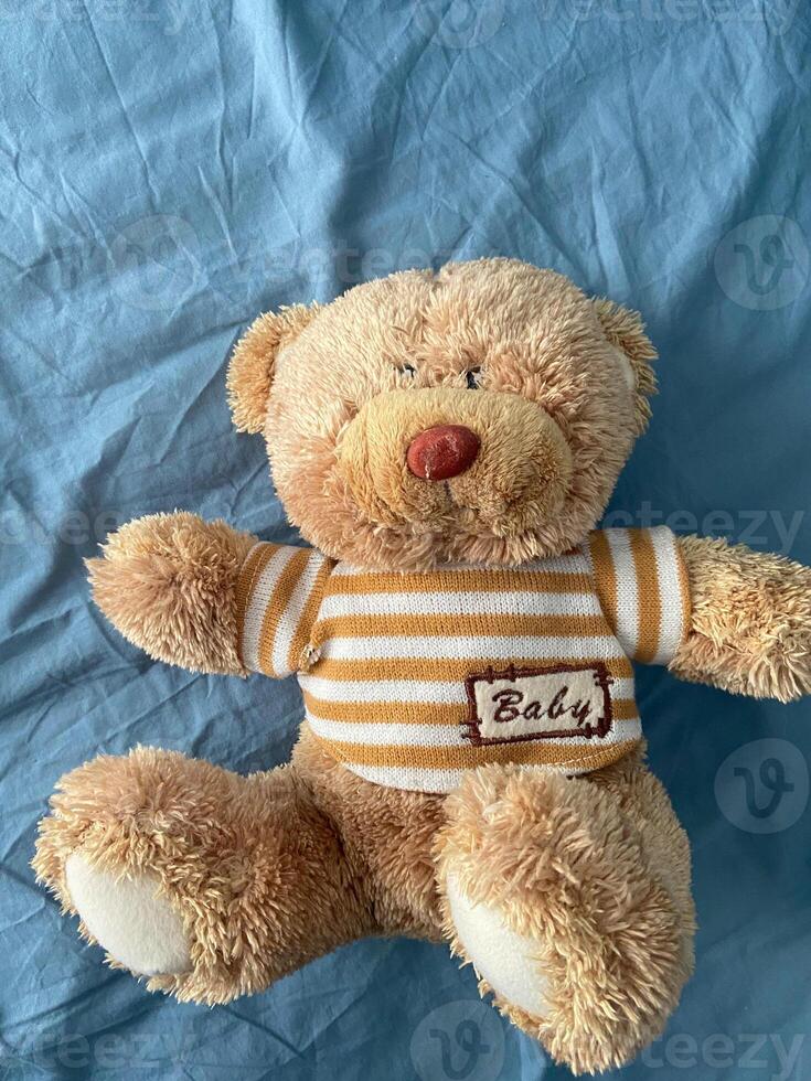 Soft and cuddly teddy bear lies on a light blue fabric surface, exuding warmth and comfort. Timeless design evokes feelings of childhood nostalgia and tranquility innocence photo