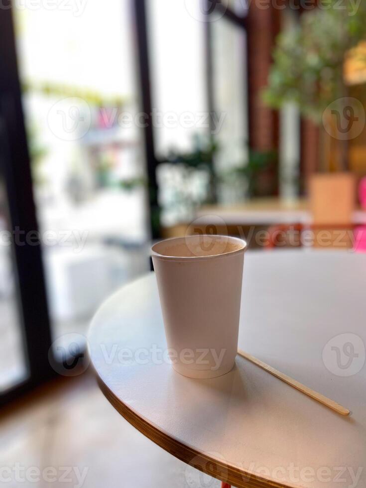 Simple white paper cup sits on a round table in a cozy cafe, inviting a moment of relaxation and warmth. Blurred background suggests a peaceful indoor setting photo