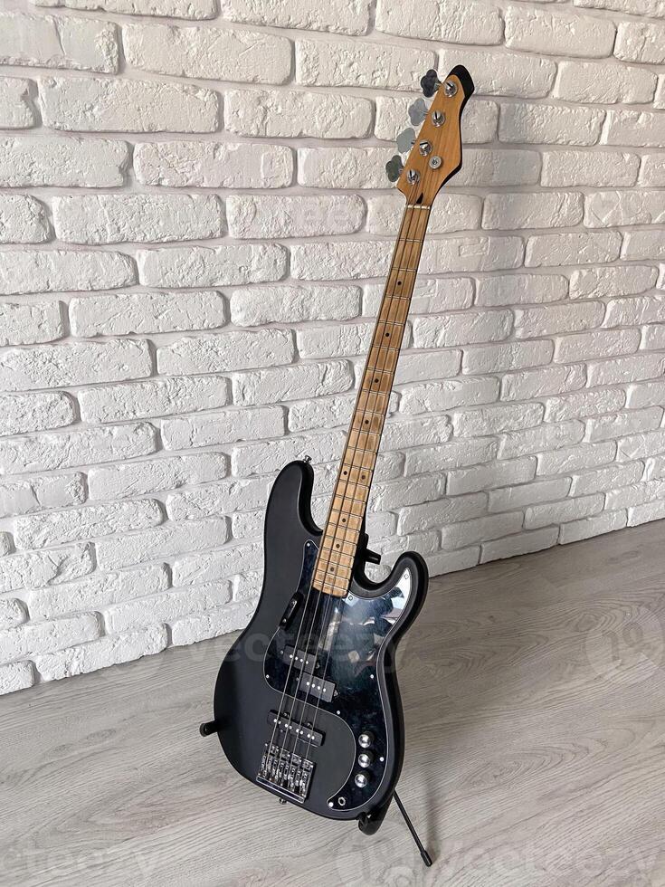 Sleek black electric bass guitar stands poised against a textured white brick wall, capturing the essence of modern music and style. The contrast between the dark instrument photo
