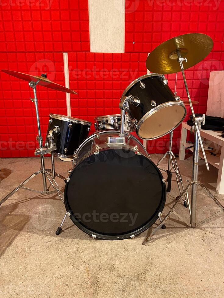 Classic black drum set is positioned in a studio with vibrant red soundproof walls. Shiny black drums and bright red background creates a dynamic and energetic music atmosphere. photo