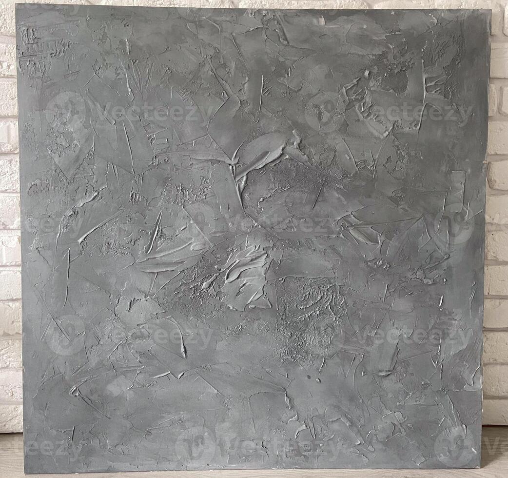 Textured gray canvas leans against a white brick wall, offering a stark contrast and highlighting the intricate details within the artwork. Artistic blend of the canvas photo