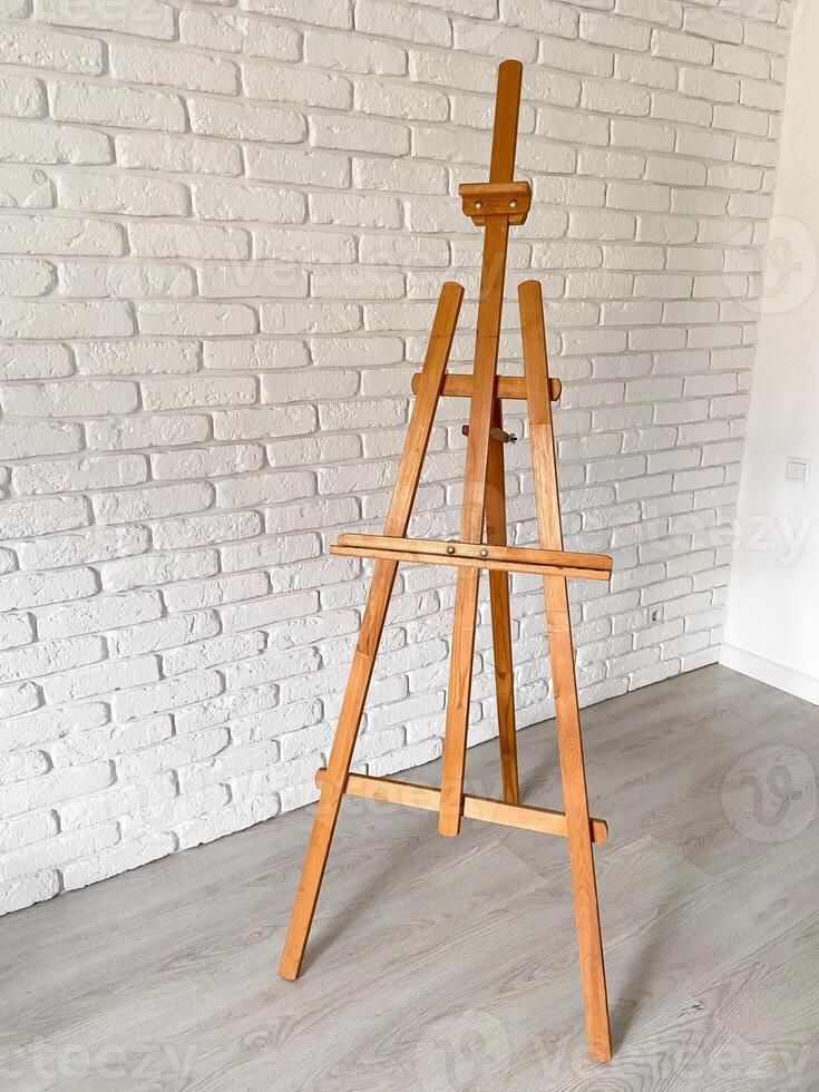 An artist's easel stands elegantly against a textured white brick wall, with well-used wooden canvas holder. Creativity and artistic expression concept photo