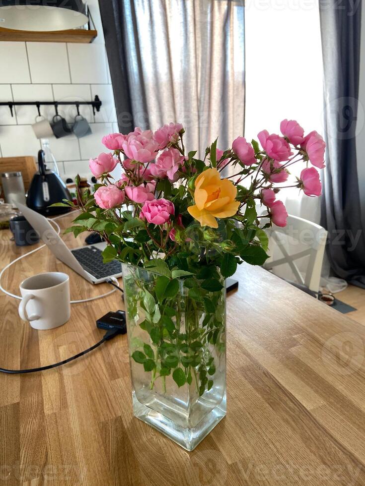 Bouquet of pink and yellow roses in a glass vase adds a touch of elegance to a modern kitchen. Natural light highlights the vibrant colors, creating a serene atmosphere photo