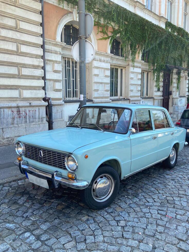 Vintage car is parked on a cobblestone street in front of a historic building adorned with creeping ivy. This classic vehicle evokes nostalgia and charm against the backdrop of timeless architecture photo