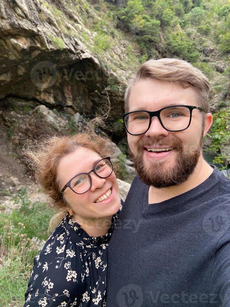 Millennial joyful couple takes a selfie in a lush, mountainous landscape, celebrating their outdoor adventure. Beauty of nature and the happiness of shared experiences photo