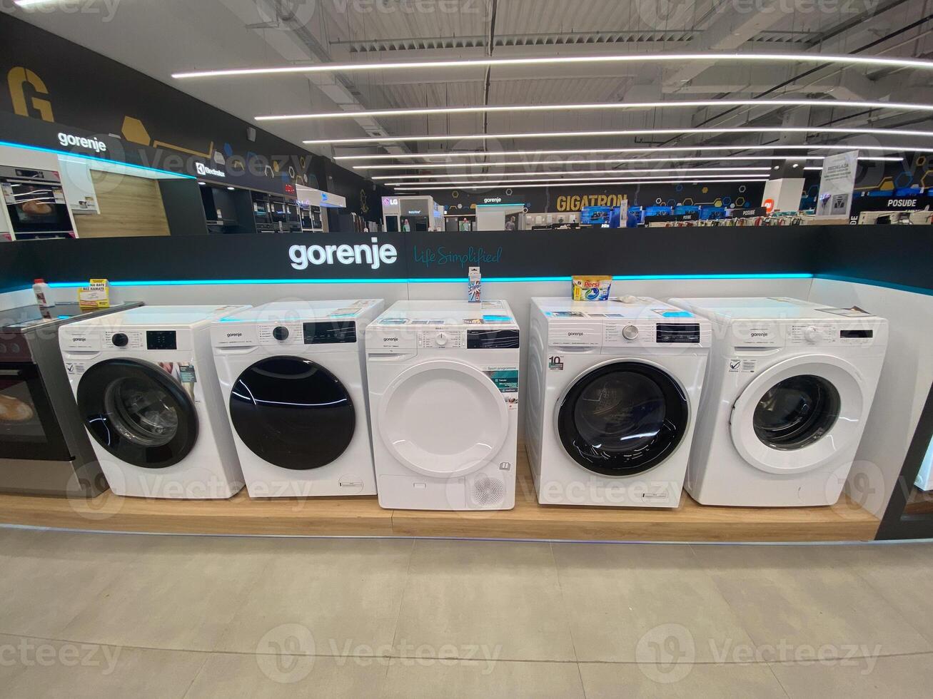 Row of modern washing machines is displayed in an electronics store, showcasing the latest models with sleek designs and advanced features. Under bright lights, photo