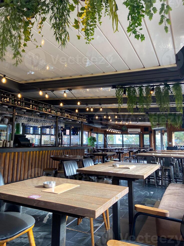 Cozy cafe interior with hanging plants and warm lighting creates a welcoming ambiance. Wooden tables and chairs are arranged neatly, inviting guests to relax and enjoy their time photo
