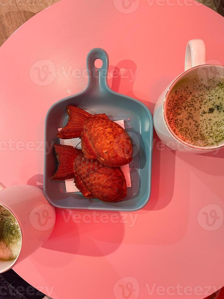 Japanese sweet Taiyaki fish shaped cake Cream filling Japan travel gourmet. Two fish shaped pastries rest on a blue dish on table with pink light, delightful culinary creativity photo