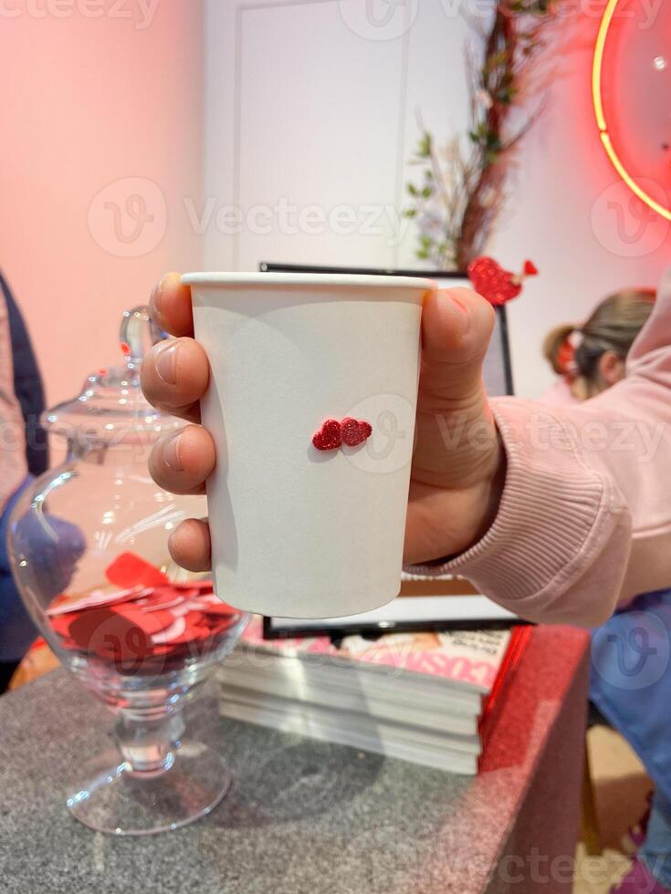 Close-up hand holds a cup of vibrant green matcha in a cozy cafe setting, Freshness of beverage. On background reveals a glimpse of the barista's workspace, filled with colorful straws and utensils photo