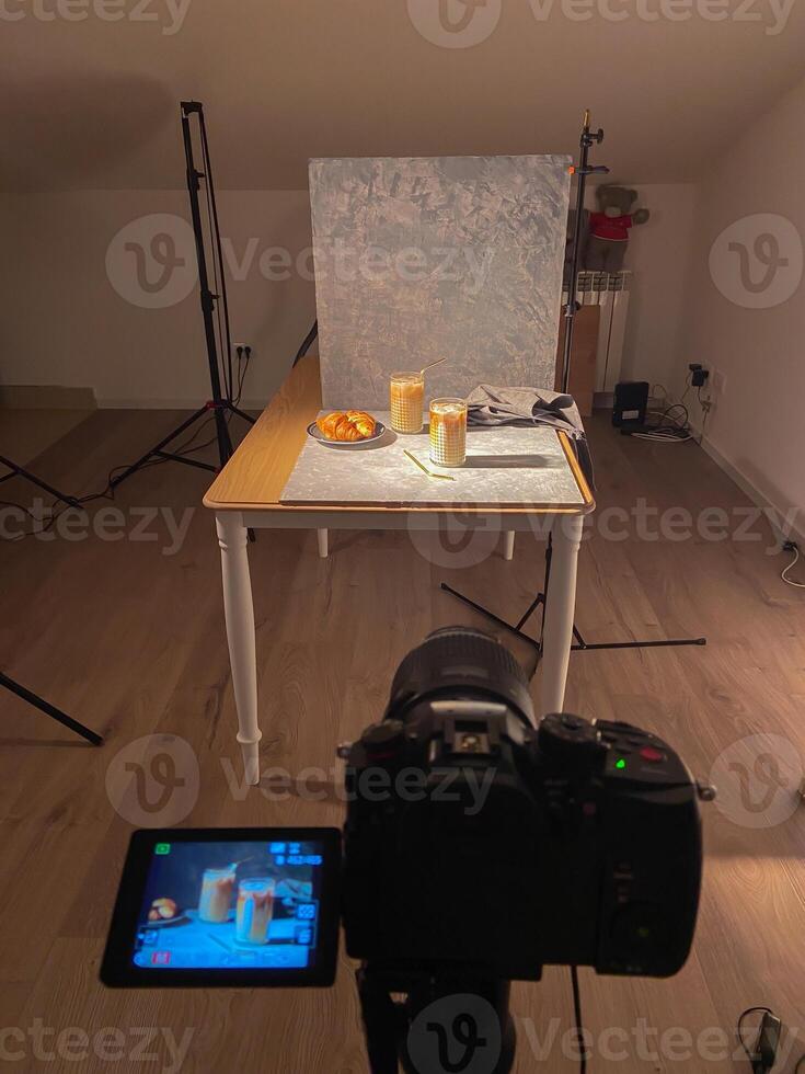 Camera setup captures a food photography scene with a cozy table arrangement, featuring pastries and drinks in a studio setting. Art of capturing culinary delights with precision and creativity photo