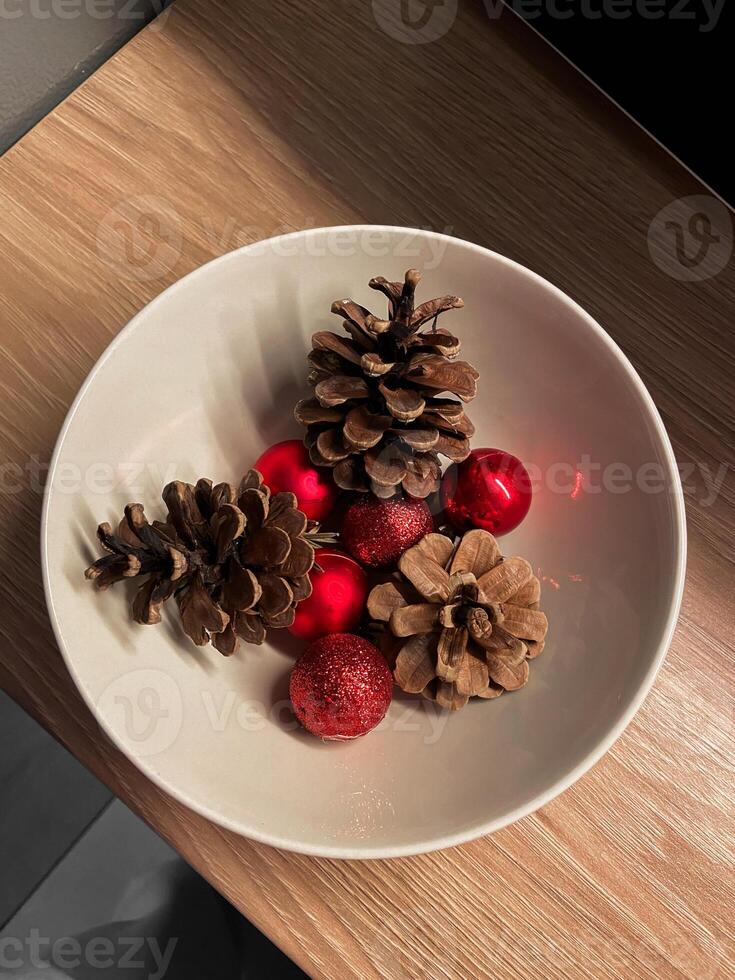 Arrangement of pinecones and red ornaments in a simple white bowl in Christmas, highlighting natural textures and festive colors. Composition captures essence photo