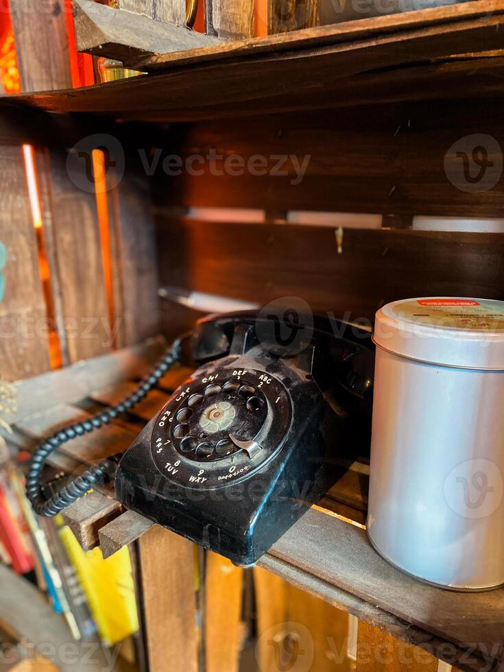 Vintage rotary phone sits on a rustic wooden shelf, accompanied by a simple metal tin. this image captures a sense of nostalgia and timeless charm, evoking memories of past eras photo