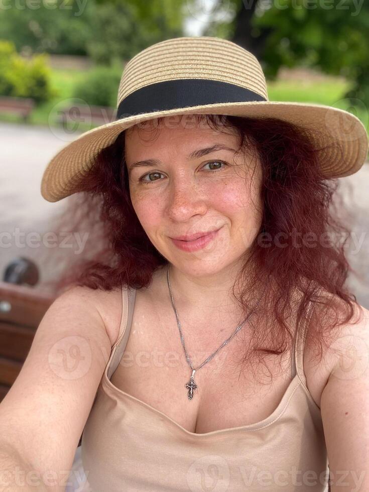 Pretty woman with freckles and curly red hair smiling outdoors and taking selfie portrait photo