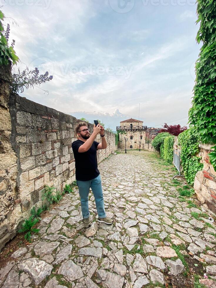 A man takes a photo while standing at a viewpoint in fortress. A tourist with a smartphone camera