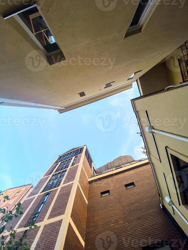 Looking up at the intersection of two modern beige buildings against a bright blue sky. Minimalist urban scene, highlighting the contrast between architecture and open sky photo