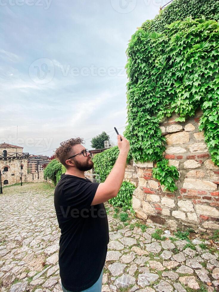 A man takes a photo while standing at a viewpoint in fortress. A tourist with a smartphone camera