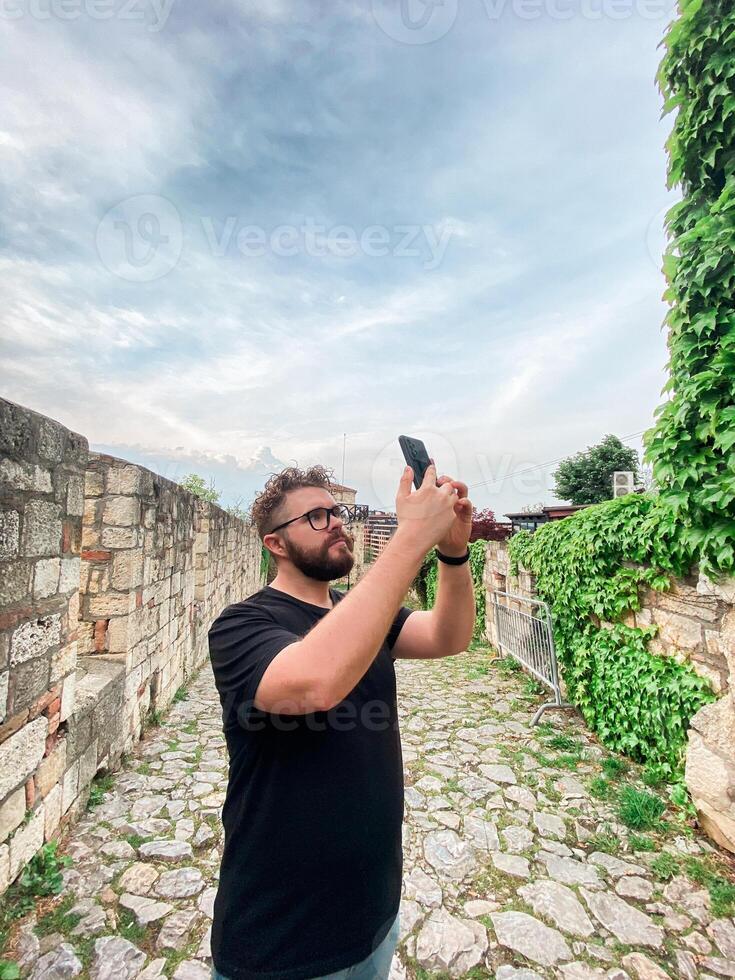 A man takes a photo while standing at a viewpoint in fortress. A tourist with a smartphone camera