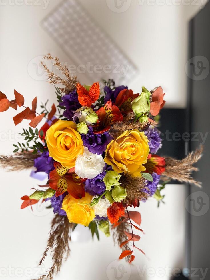 Colorful bouquet of flowers in a lavender box standing on a desk, tied with a vibrant red and purple ribbon. Bright, mixed arrangement adds a touch of nature and warmth to modern workspace photo