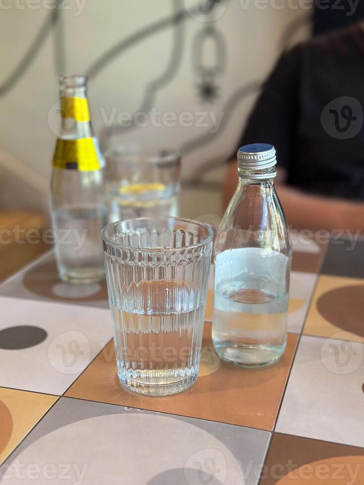 Glass of water alongside a bottle on a patterned tile table. Depicting everyday hydration and minimalistic lifestyle themes. photo
