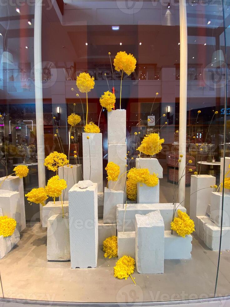 Modern art display featuring tall concrete blocks with vibrant yellow flowers arranged atop them. Contrast of industrial materials with natural elements creates photo