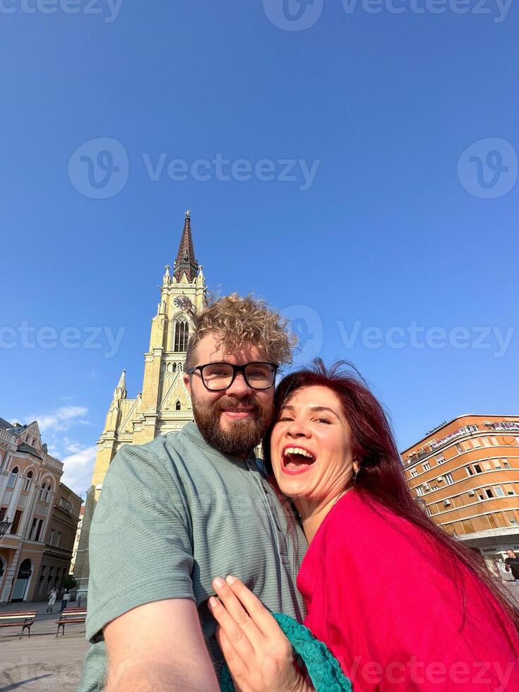 Funny couple taking a selfie in front of a historical building on a sunny day, with clear blue sky and impressive architecture. capturing moments of travel and togetherness photo