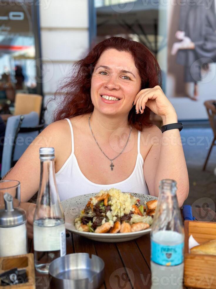 Young woman sitting in summer cafe, eating dish with meat and parmesan cheese. Travel, tourism, food and drink. photo