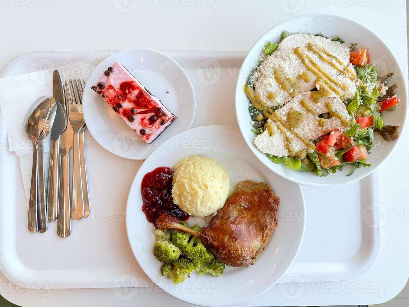 Delicious meal with duck leg, mashed potatoes, salad, and dessert served on a white tray. Vibrant and appetizing food arrangement for lunch or dinner photo