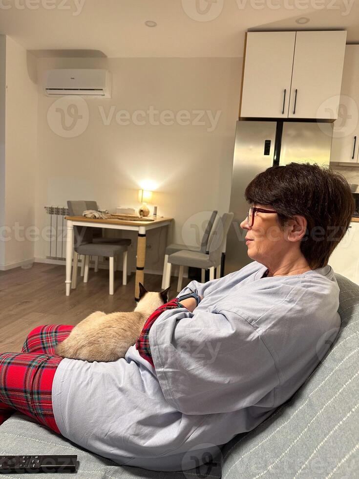 Woman relaxing at home with a cozy cat. Warmth of companionship and tranquility in a modern living room. Home comfort, bonding with a pet and evening relaxation photo