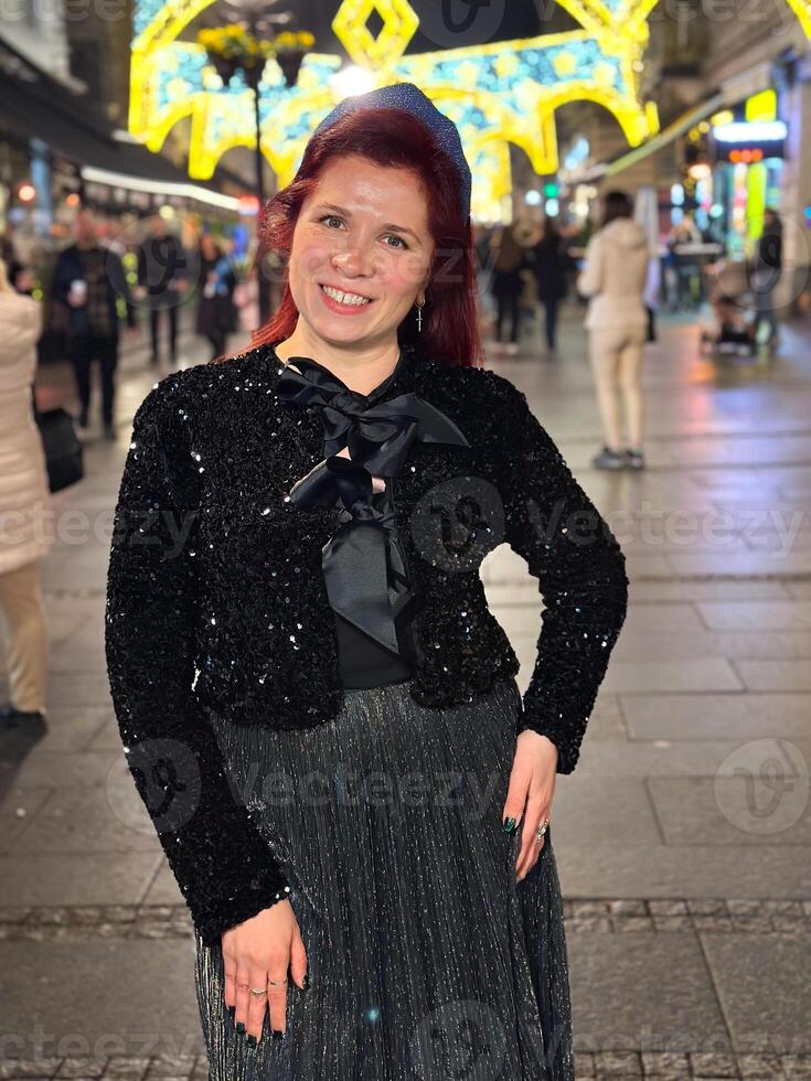 Millennial woman standing outdoors at Christmas night,. City lights in the background create a warm and Christmas holidays atmosphere, enhancing the peaceful and confident expression on her face photo