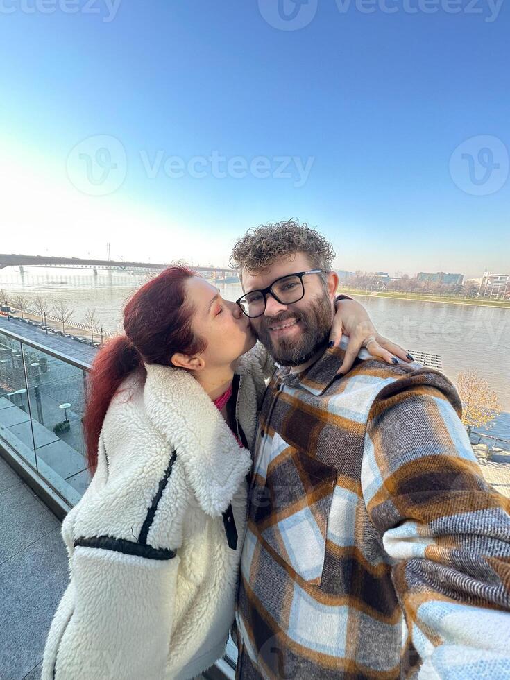 Man and woman taking selfie in cold time outdoor. Couple enjoying a beautiful day by the river with a breathtaking view. Moment of connection and joy together photo