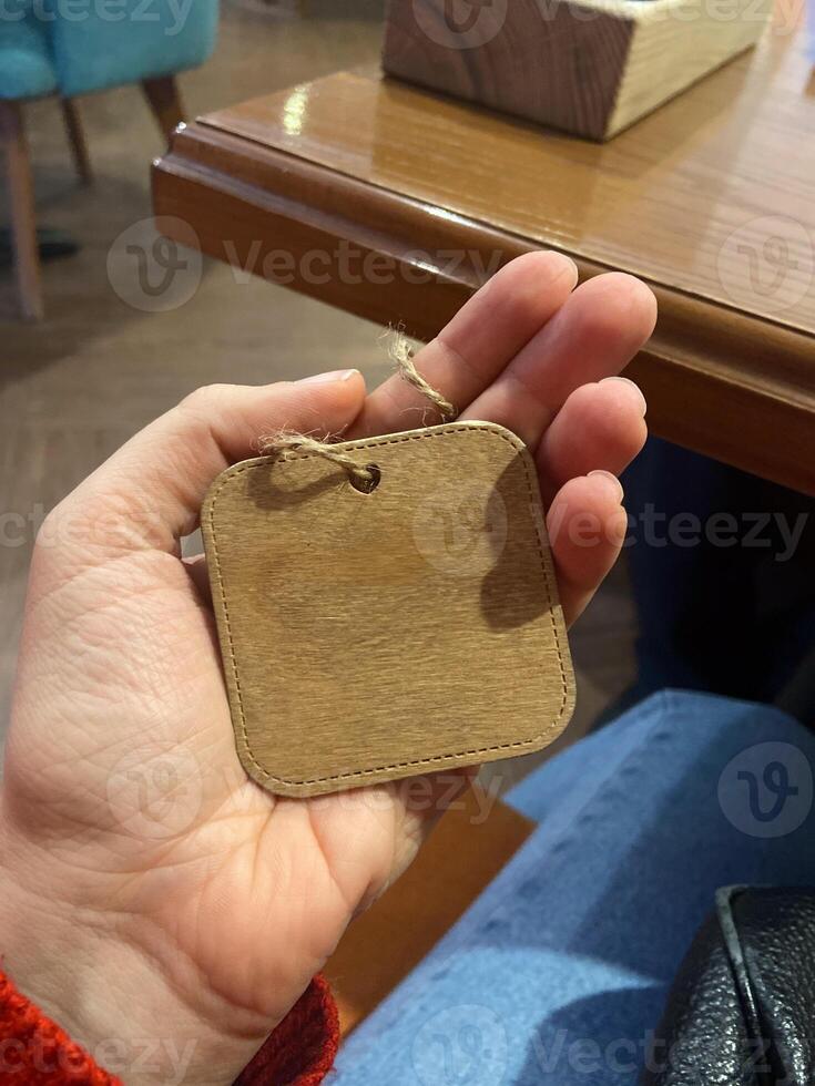 Close-up hand holds a small wooden tag with a twine loop. Copy space and empty place for text. Natural texture and simplicity of the tag create a connection to artisanal craftsmanship photo