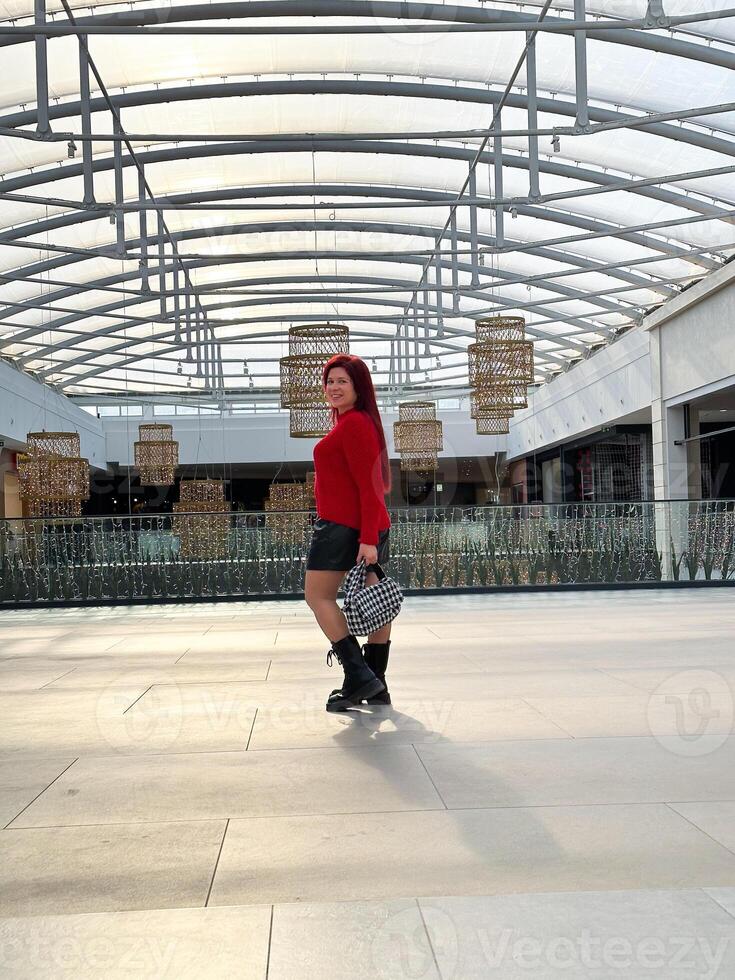 Millennial woman poses confidently in an open, modern environment, wearing a vibrant red sweater and black boots. photo