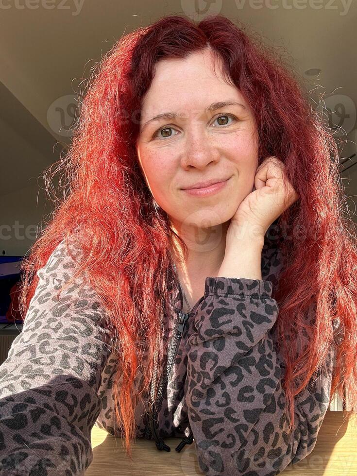Portrait smiling woman with vibrant red hair basks in the glow of sunlight. her relaxed expression and comfortable attire create an atmosphere of warmth and contentment. photo