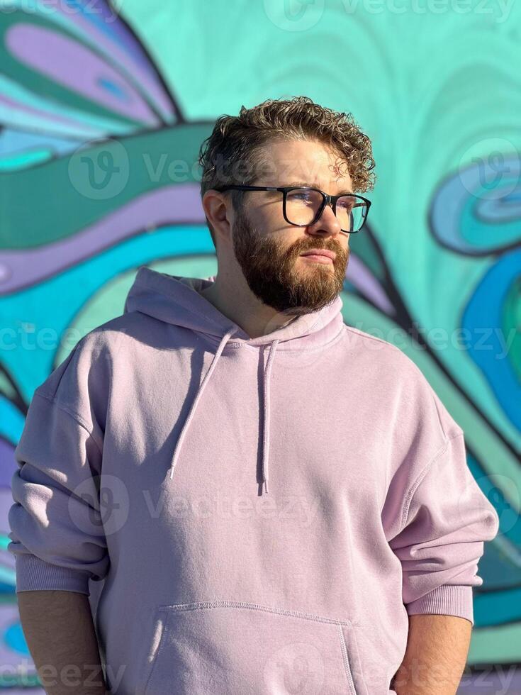 Millennial man in a pastel hoodie standing in front of a vibrant, abstract mural. Soft fabric and bold graffiti creates a striking contrast of modern urban style. Street urban style fashion photo