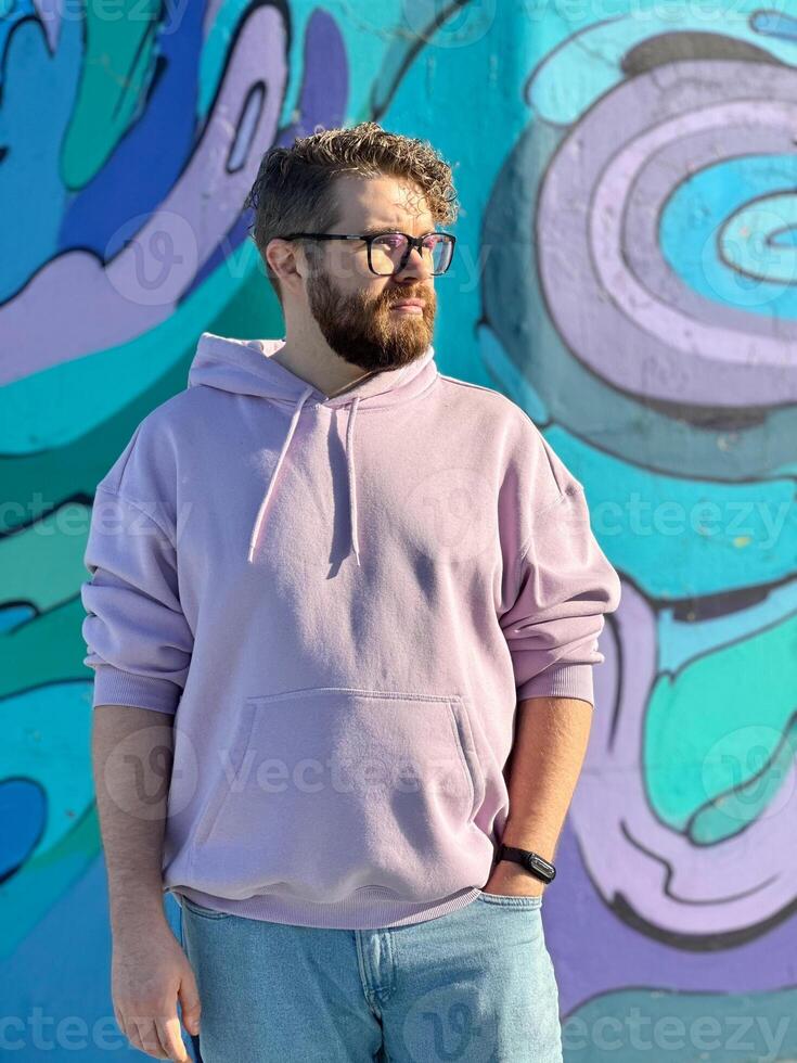 Millennial man in a pastel hoodie standing in front of a vibrant, abstract mural. Soft fabric and bold graffiti creates a striking contrast of modern urban style. Street urban style fashion photo
