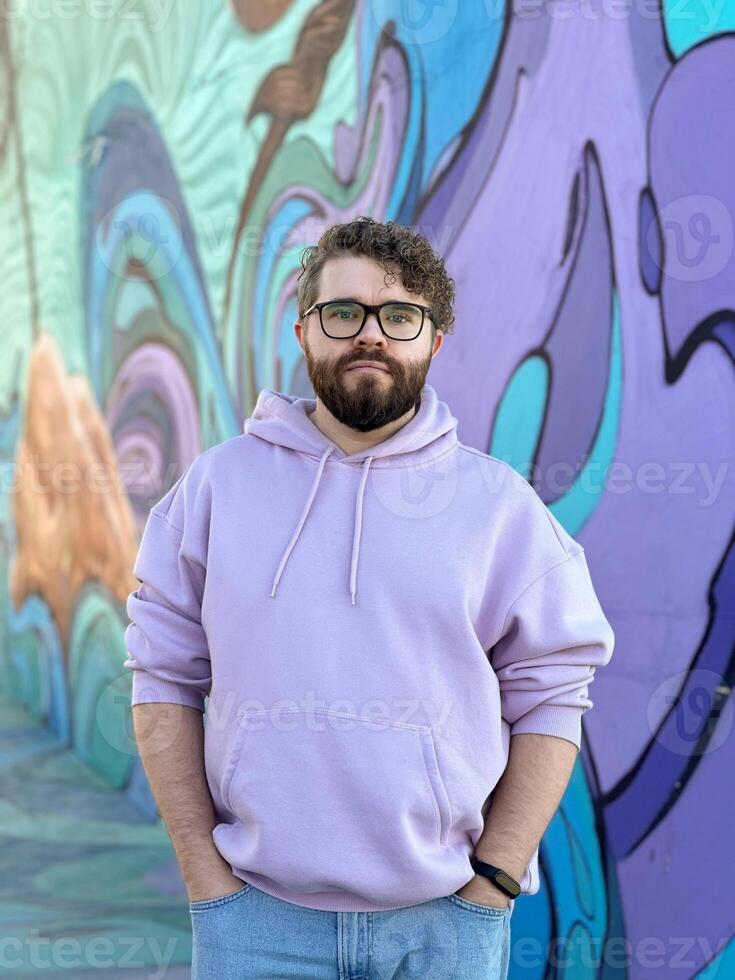 Millennial man in a pastel hoodie standing in front of a vibrant, abstract mural. Soft fabric and bold graffiti creates a striking contrast of modern urban style. Street urban style fashion photo