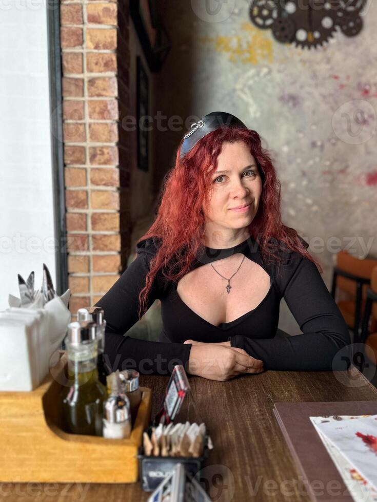Millennial woman with red hair sits thoughtfully at a rustic cafe table, surrounded by a cozy and artistic atmosphere. Soft lighting and her pensive expression convey photo