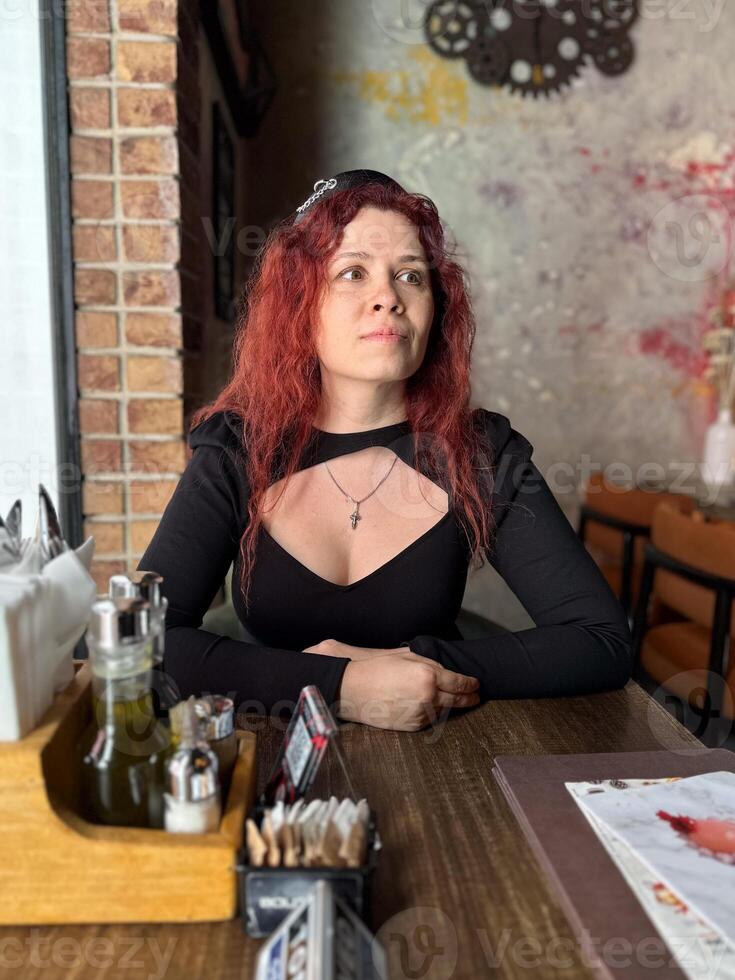 Millennial woman with red hair sits thoughtfully at a rustic cafe table, surrounded by a cozy and artistic atmosphere. Soft lighting and her pensive expression photo