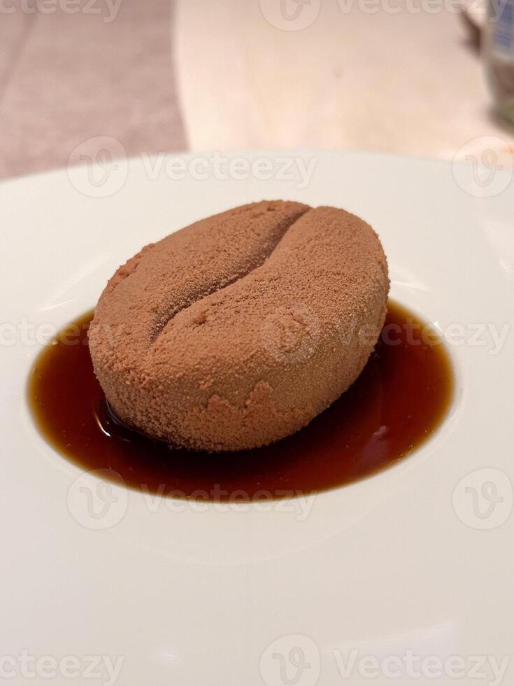 Close-up delicately crafted dessert resembling a coffee bean rests on a plate, surrounded by a rich brown sauce. Creative culinary presentation combines texture photo