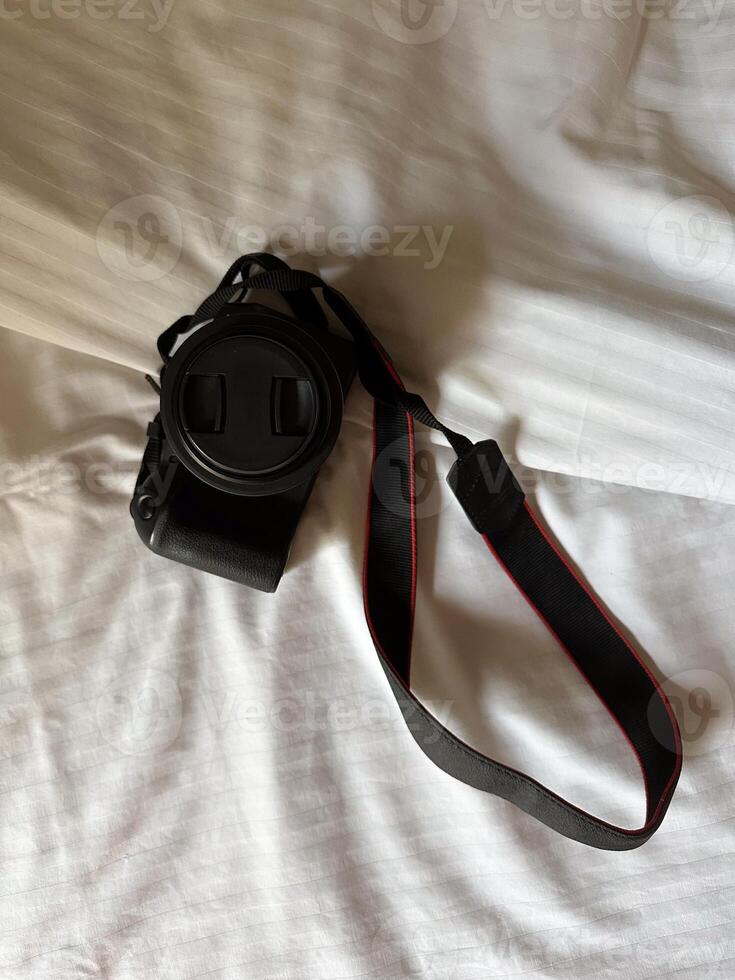 Camera with a strap placed on a white bed sheet, capturing the essence of travel preparation and creativity. Simplicity, creative and readiness of a photographer journey. Top view photo