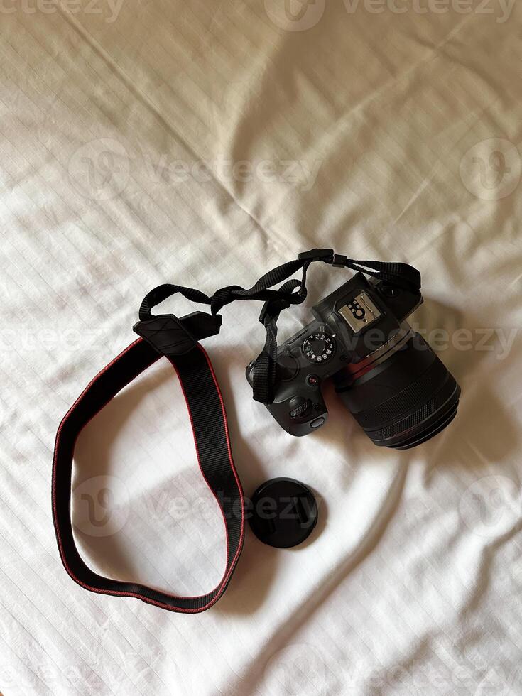Camera with a strap placed on a white bed sheet, capturing the essence of travel preparation and creativity. Simplicity, creative and readiness of a photographer journey. Top view photo